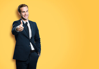 Excited businessman showing thumb up like sign gesture, in black confident style suit, on vivid yellow background. Handsome happy man. Copy space for slogan or text.