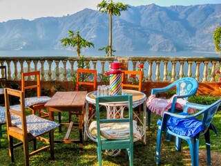 A charming rustic setting, with mismatched tables and chairs set for a morning tea break, overlooking Lake Phewa in Pokhara, Nepal.