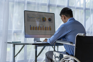 Asian male businessman working in office sitting on wheelchair doing financial work with graphs on...