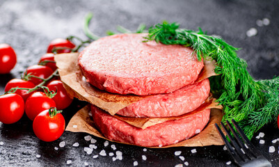 Raw burger on a table with greens and salt. 