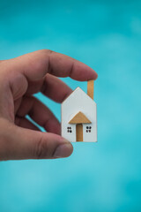 A model of a house made of wood on a hand against on a blue background. Building or property concept. Home for family dream or rent and sold.