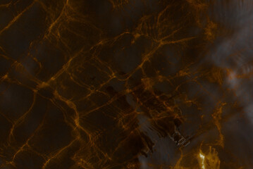 An abstract photo of the texture of light reflections from a transparent water surface and waves in dark orange tones.