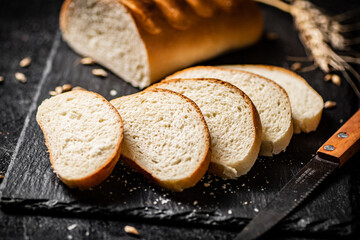 Sliced wheat bread with a knife on a stone board. 