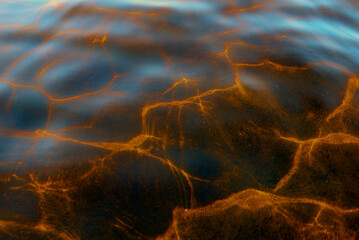 Abstract photo of the texture of the reflection of light from the surface of the water waves of the river from the sky in bright yellow tones. The background is magical.