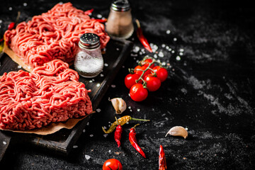 Raw minced meat on a cutting board with cherry tomatoes. 