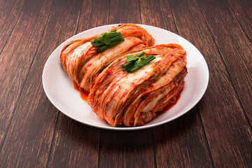 Korean kimchi. Korean traditional cabbage kimchi on white plate. Wood deck background, closeup.