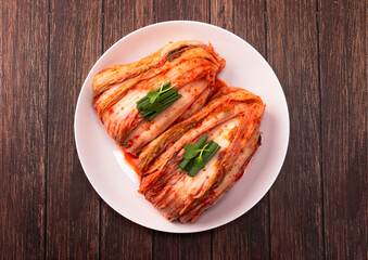 Korean kimchi. Korean traditional cabbage kimchi on a white plate viewed from above. Wood deck background, closeup.