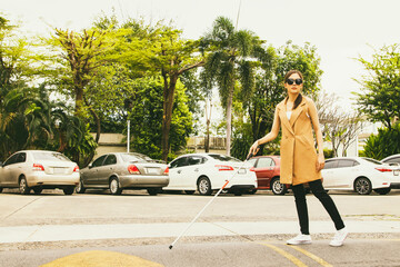 Beautiful blind asian woman crosses the road using cane to guide the walk slowly for safety while...