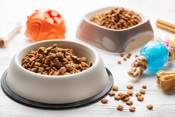 A bowl with dog food, dog treats and toys on a wooden floor.