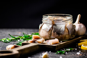 Salted herring in a jar on a cutting board with rosemary and lemon. 