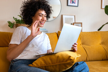 Happy African American woman waving hand during a video call at home sitting on the sofa says hi to a friend.Copy space.