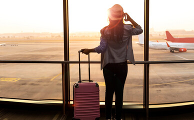 Happy explore travel concept with young tourist woman holding the luggage and looking the airplane in the hall room with sunlight at the airport