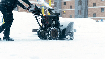 a janitor on a snowplow removes snow in the courtyard of a residential building