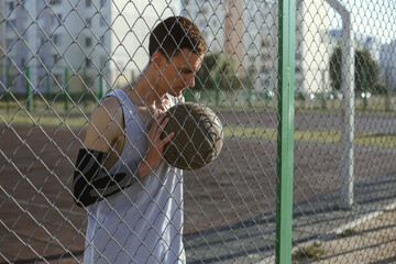 Young male streetball player with ball standing on basketball urban court in summer 