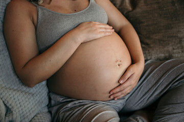 Close up of mother to be cradling her belly sitting on the sofa