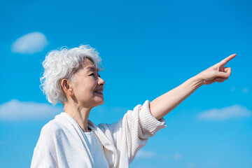 青空の下で未来を指差すシニアの女性