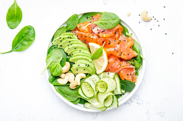 Salmon salad for ketogenic diet with avocado, spinach, cucumber, cashew nuts. Low-carbohydrate lunch rich in healthy fats. White table background, top view