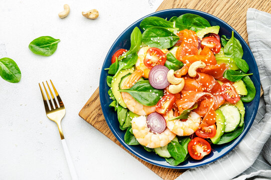 Ketogenic diet salad with salmon, shrimp, avocado, spinach, cucumber, tomato, cashew nuts, sesame. Low-carbohydrate lunch rich in healthy fats. White table background, top view