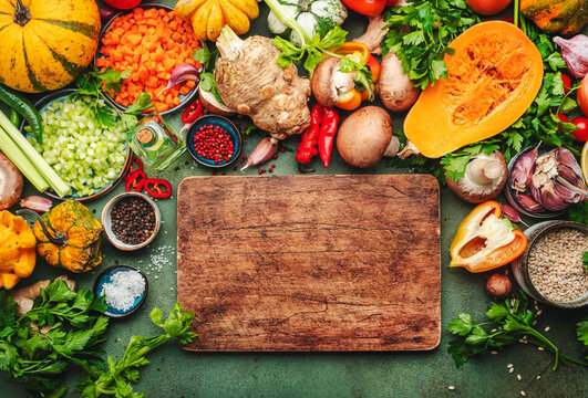 Food background. Rustic wooden cutting board. Vegetables, mushrooms, roots, spices - ingredients for vegan cooking. Healthy eating, diet, comfort slow food. concept. Old kitchen table, top view