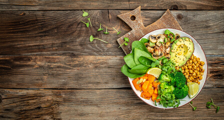 vegetable vegetarian buddha bowl avocado, mushrooms, broccoli, spinach, chickpeas, pumpkin on a wooden background. Long banner format. top view