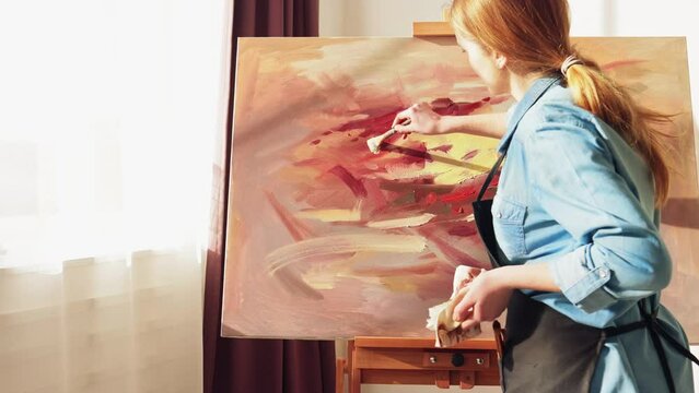 Zoom in. Woman artist painting in art studio. Talented Female Artist Walks to a Canvas and Starts Working on a Modern Abstract Oil Painting Using Paintbrush. Slow motion.