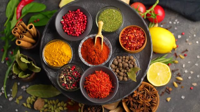 Set of Spices and herbs for cooking. Small bowls with colorful seasonings and spices - basil, pepper, saffron, salt, paprika, turmeric. On black stone table top view copy space
