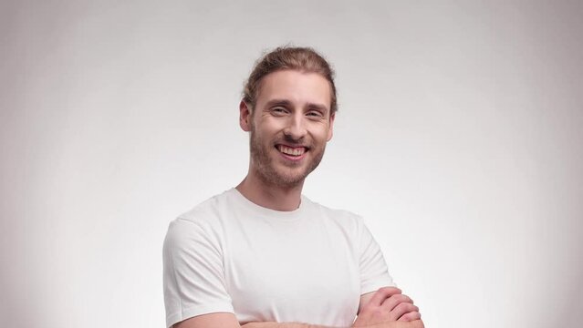 Happy Handsome boy touches his face, hair and looks at the camera. Young Caucasian blond curly male in casual clothing posing isolated on white background in studio straightens his hair.