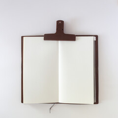 Open white blank on white background with plastic paper clip. Travel notebook or sketchbook.
