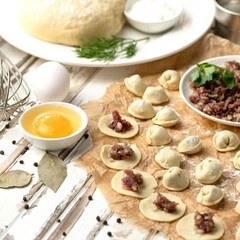 Meat dumplings on wooden table. Process of making dumplings. Stuffing from minced meat. Ingredients for dough, spices, herbs. Ready-made semi-finished products and not pinched.
