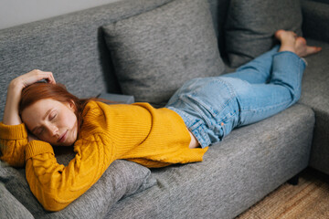 High-angle view of peaceful young woman with serene face relax at home lying down in comfortable sofa couch, enjoy welfare peace of mind. Happy female sleeping on stomach in cozy living room.