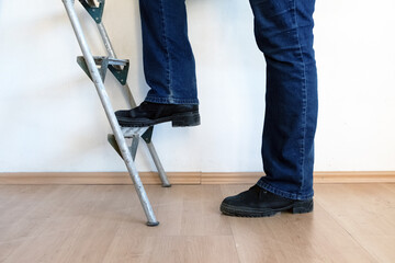 Legs in jeans and black boots climb a dirty building ladder