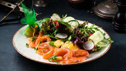 Green salad with salmon fish, cucumbers, lettuce, radish, arugula and spices.