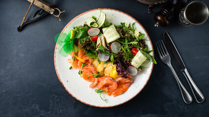 Salad with salmon fish, cucumbers, lettuce, radish, arugula and spices.