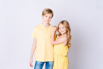 Two happy children standing near an empty gray background and hugging cute little girl with long hair is hugging cute blonde girl showing her love and care Brother and sister have fun posing in studio