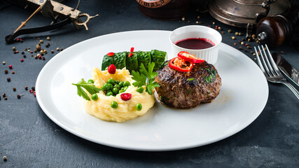 Beef cutlet with mashed potatoes, green peas, cucumber, chili and lingonberry sauce.