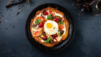 Fried big potato pancake with champignon mushrooms, tomatoes, egg, onion, herbs and sour cream in a frying pan.