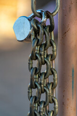 Linked chain locked together with pad made of metal and hanging on ring on a post in late afternoon shade