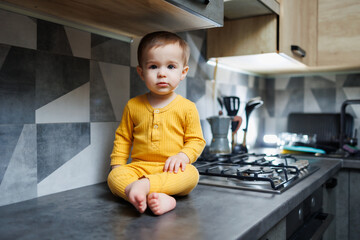 A little boy 1 year old in yellow clothes is sitting in the kitchen on the table. Portrait of a...