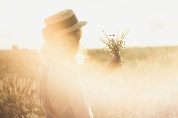 Close up girl in straw hat with bouquet surrounded by sunlight glare concept photo. Side view...