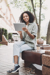 Smiling young woman using digital tablet in a city. Beautiful student girl having coffee break. Modern lifestyle, connection, business, freelance work concept