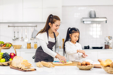 Obraz na płótnie Canvas Portrait of enjoy happy love asian family mother and little toddler asian girl daughter child having fun cooking together with dough for homemade bake cookie and cake ingredient on table in kitchen