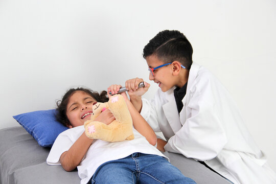 Latino Girl And Boy Play To Be A Doctor With A White Coat That Is Too Big For Her And Patient Who Acts To Feel Sick Very Entertaining And Funny They Make Jokes
