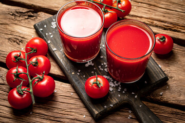 Glasses with tomato juice on a wooden cutting board. 