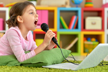 Adorable little girl singing karaoke with laptop