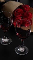 Romantic Dinner. two glasses of red wine  on black desk, Bouquet of flowers lying on the table, selective focus on bunch of roses
