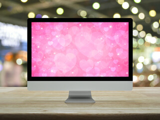 Desktop modern computer monitor with pink love heart screen on wooden table over blur light and shadow of shopping mall, Business internet dating online, Valentines day concept