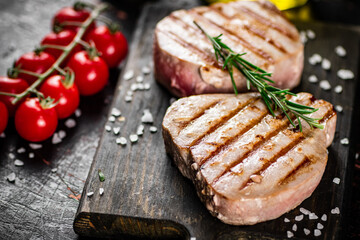 Grilled tuna steak on a cutting board with spices, tomatoes and rosemary. 