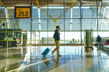 Full length view of young hispanic man traveling at airport hallway with luggage