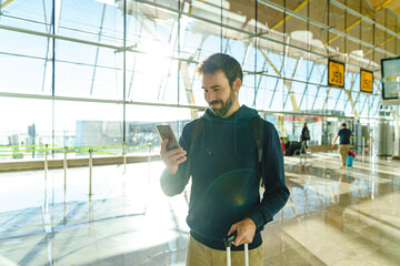 Portrait of caucasian young man using phone at airport hall at sunset