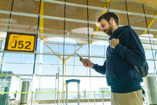 Mid waist portrait of caucasian young man using phone at airport check in at sunset